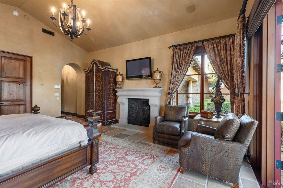 Refined bedroom seating area with luxurious armchairs, a decorative fireplace, and abundant natural light.