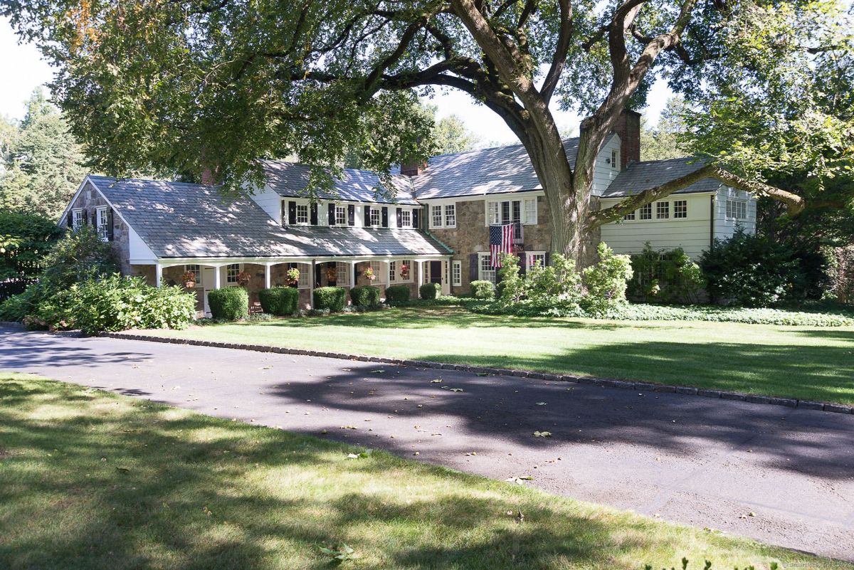 Classic colonial home with a stone facade, shaded by mature trees, and a welcoming front porch.