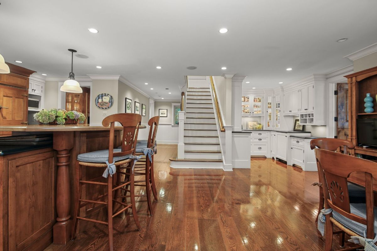 Open-concept kitchen and dining area showcasing rich hardwood floors, custom cabinetry, and a seamless transition to the staircase and additional living spaces.