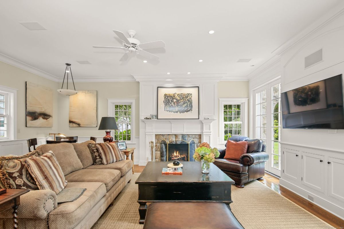 Living room featuring a stone fireplace, elegant wall paneling, and cozy furnishings under bright recessed lighting.