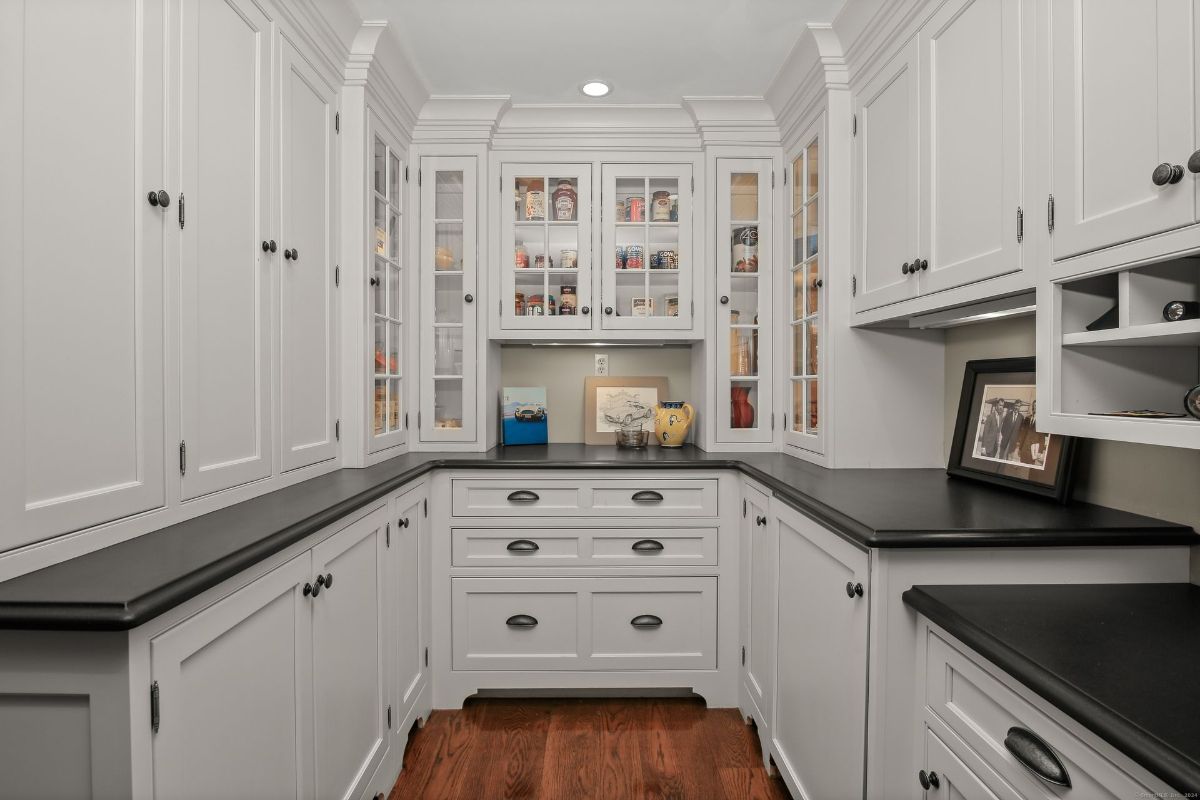 Pantry with custom cabinetry, glass-fronted displays, and sleek black countertops for a modern yet classic touch.