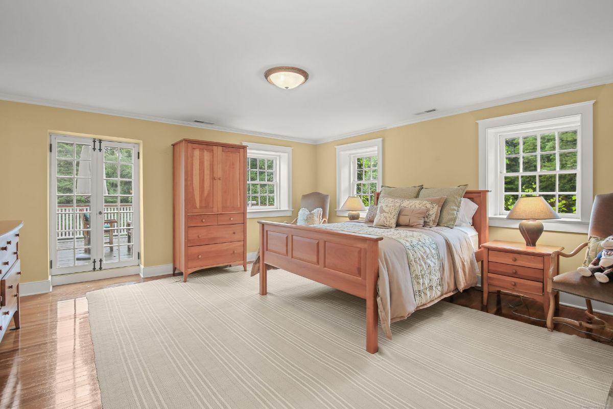 A spacious bedroom with warm yellow walls, natural wood furniture, and French doors leading to a private balcony.