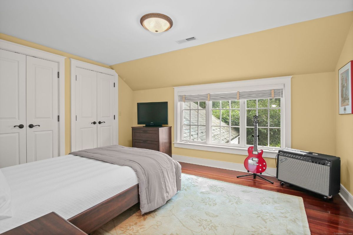 Bedroom with warm yellow walls, a cozy corner for music featuring a red electric guitar and amp, and a large window overlooking serene greenery.