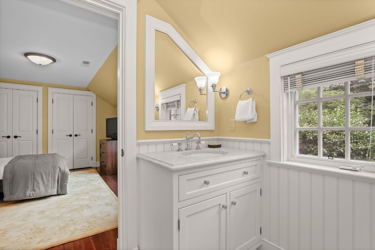 Compact bathroom with a white vanity, beadboard wainscoting, and a sunny window framing lush greenery.