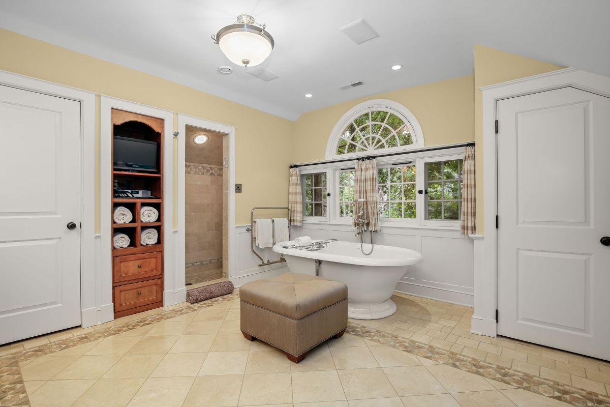 Bathroom with a freestanding soaking tub, arched window, and built-in shelving for a luxurious retreat.