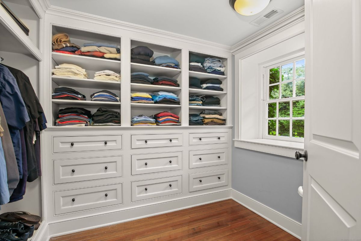 Custom-built closet with ample shelving, drawers, and natural light streaming through a charming window.