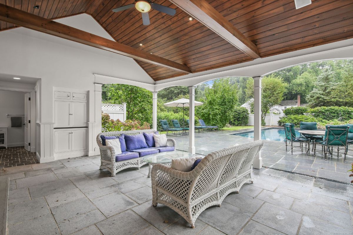 Covered poolside lounge with wicker seating, vaulted wood ceiling, and a view of the patio and pool.