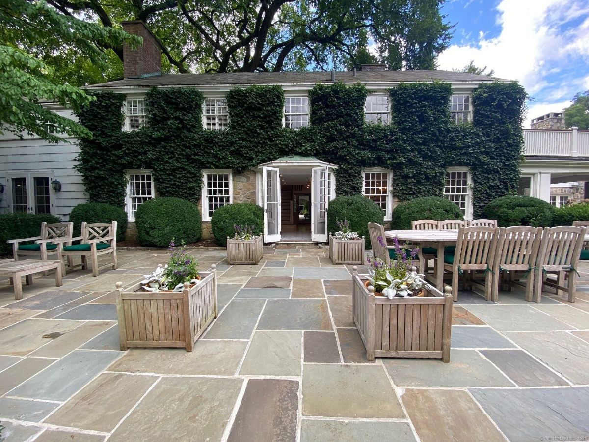 Charming ivy-clad home with a spacious stone patio, wooden planters, and elegant outdoor seating.