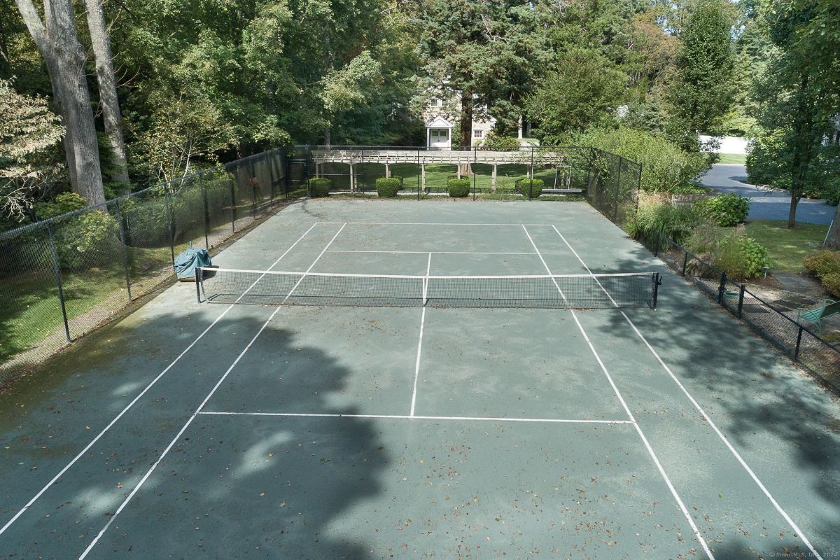 Private tennis court surrounded by lush greenery and fencing.