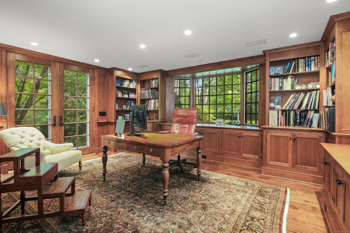 Home office featuring custom wood built-ins, expansive windows, and a luxurious leather chair overlooking serene greenery.