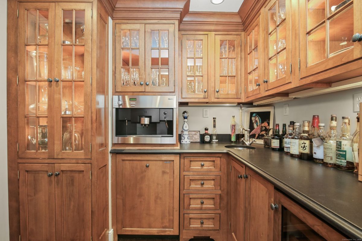 Wet bar featuring custom wood cabinetry, glass display shelves, and a built-in coffee station.