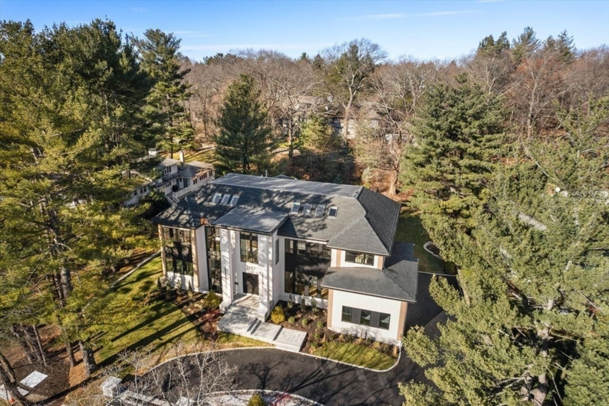 An aerial view showcasing a modern luxury home surrounded by mature trees in a serene wooded setting.