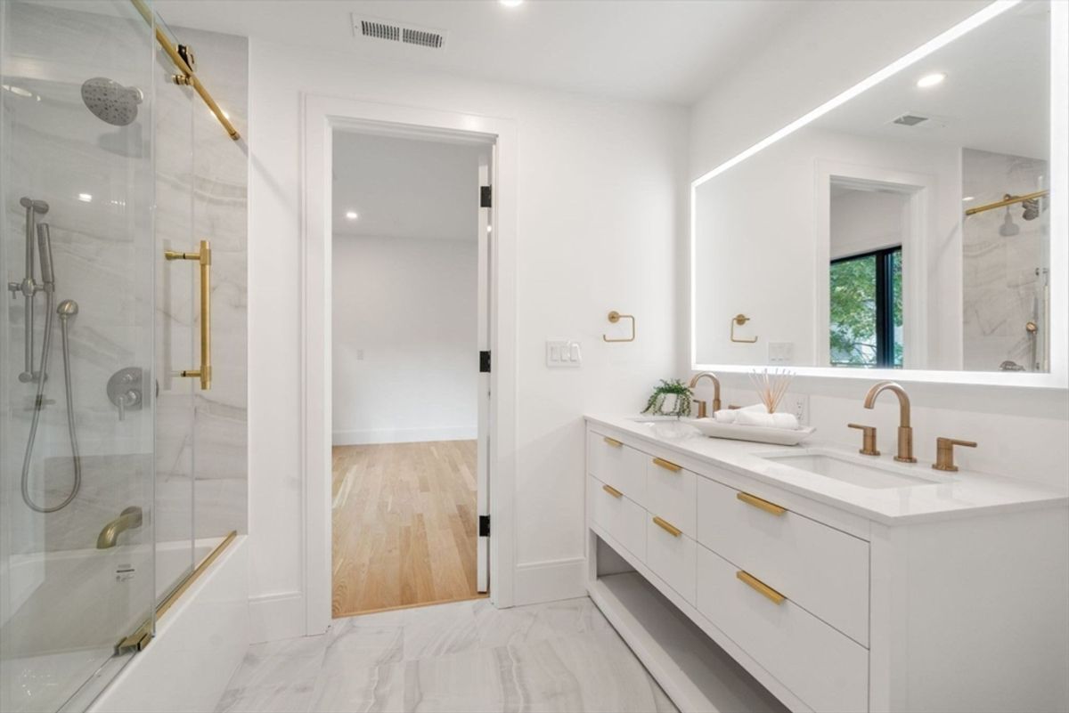 Bathroom featuring a double-sink vanity with gold hardware, a walk-in glass shower, and marble-patterned flooring.