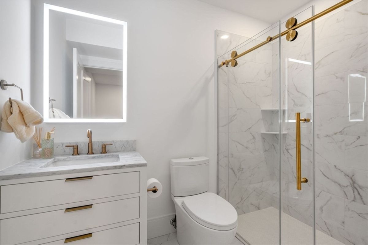 Compact bathroom with marble-patterned tiles, a sleek illuminated mirror, and gold-accented fixtures.