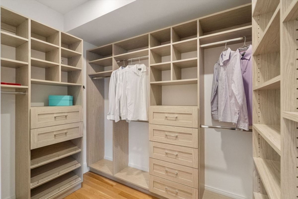 Custom-designed walk-in closet showcasing ample shelving, drawers, and hanging space in a light wood finish.