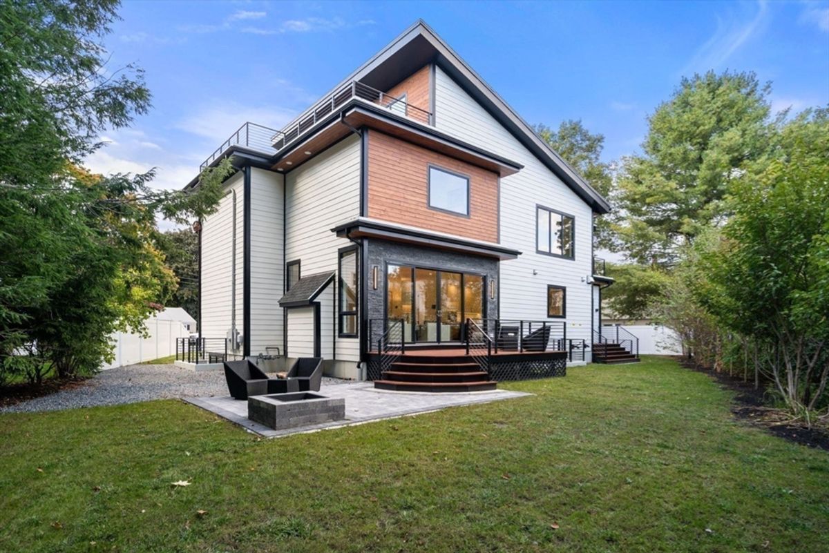 Expansive backyard features a patio with a fire pit, a wooden deck, and contemporary siding accented by wood and black trim.