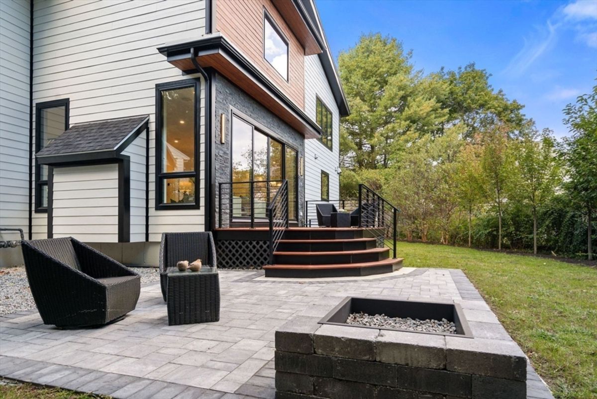 Patio area showcasing a cozy seating arrangement, stone fire pit, and steps leading to a modern deck with glass doors opening into the home.