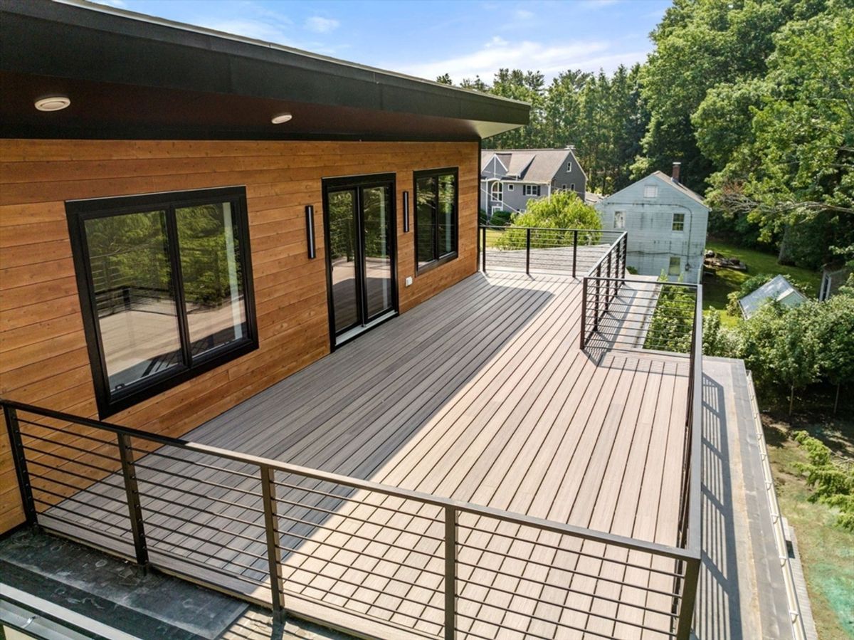 Upper deck with sleek metal railing, wood paneling, and glass doors providing seamless indoor-outdoor flow.