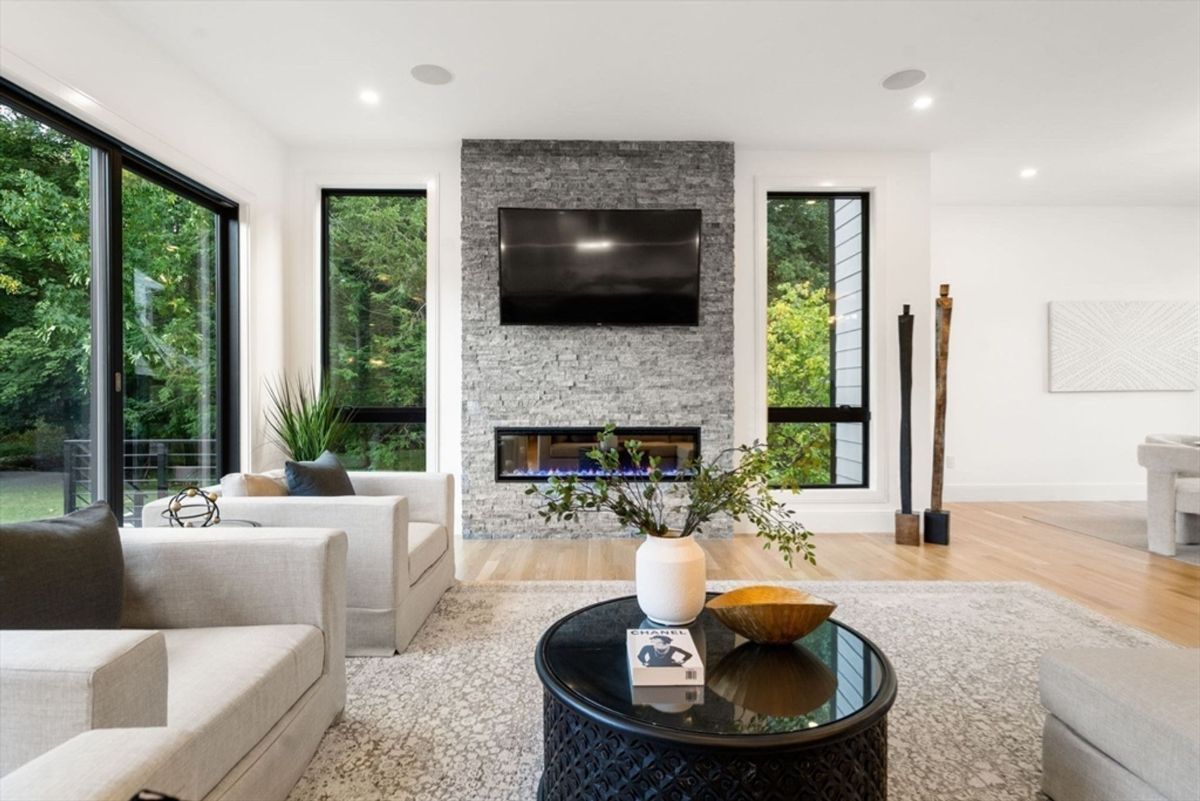 Living area features a textured stone fireplace, modern decor, and expansive windows framing lush greenery.