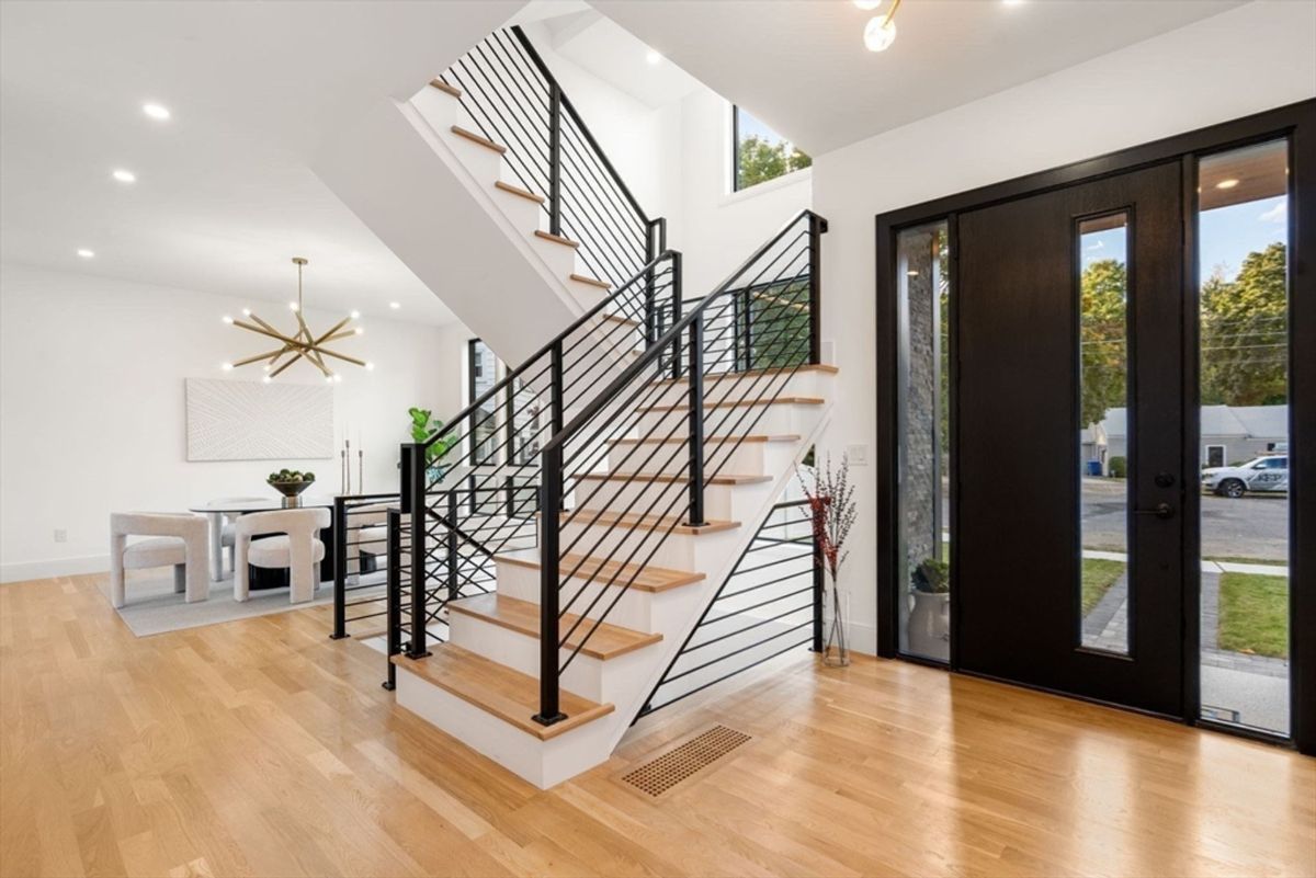 Open entryway features modern railings, warm wood flooring, and natural light flowing through large windows.