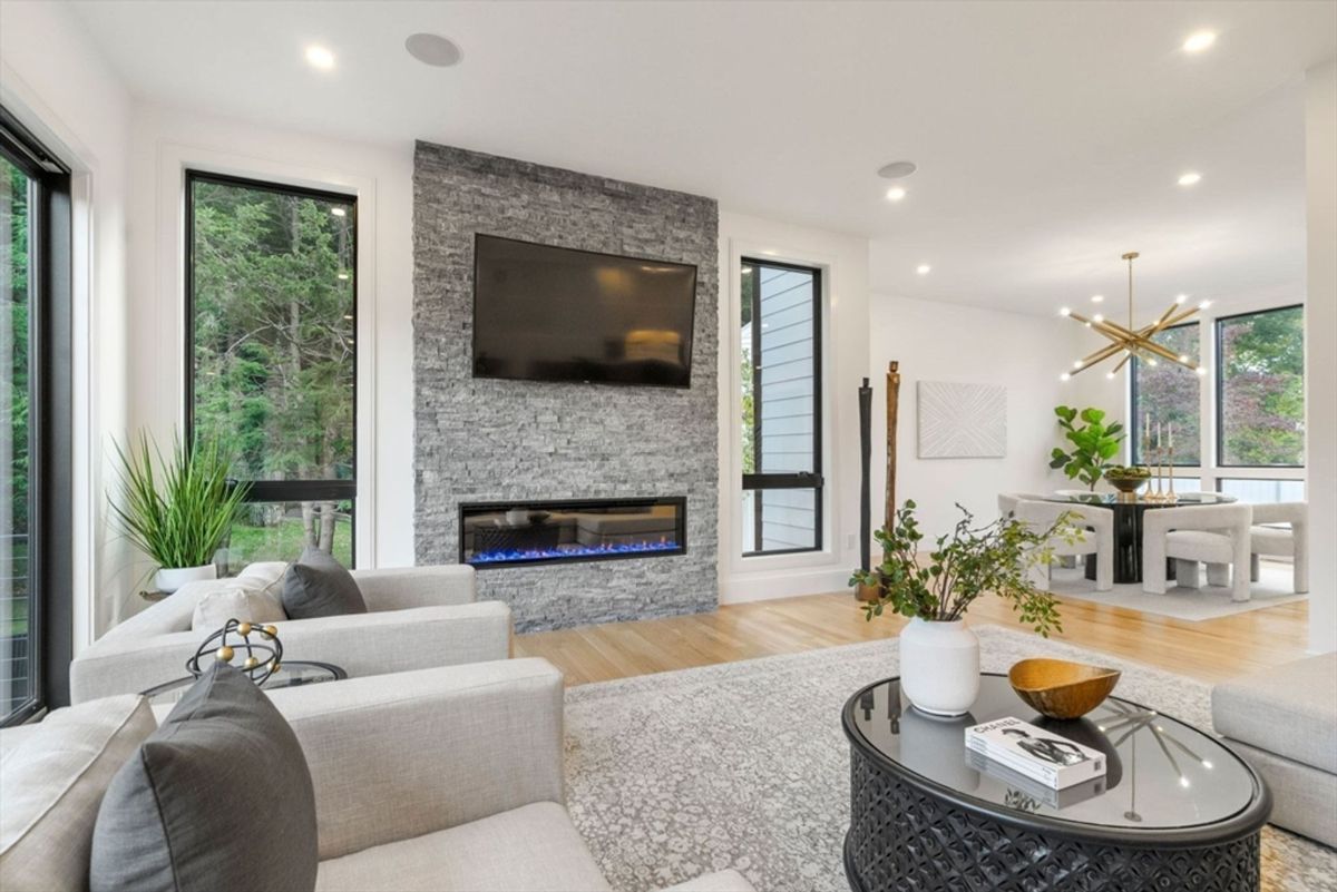 Contemporary living room showcases a sleek stone fireplace, floor-to-ceiling windows, and seamless flow into the dining area.