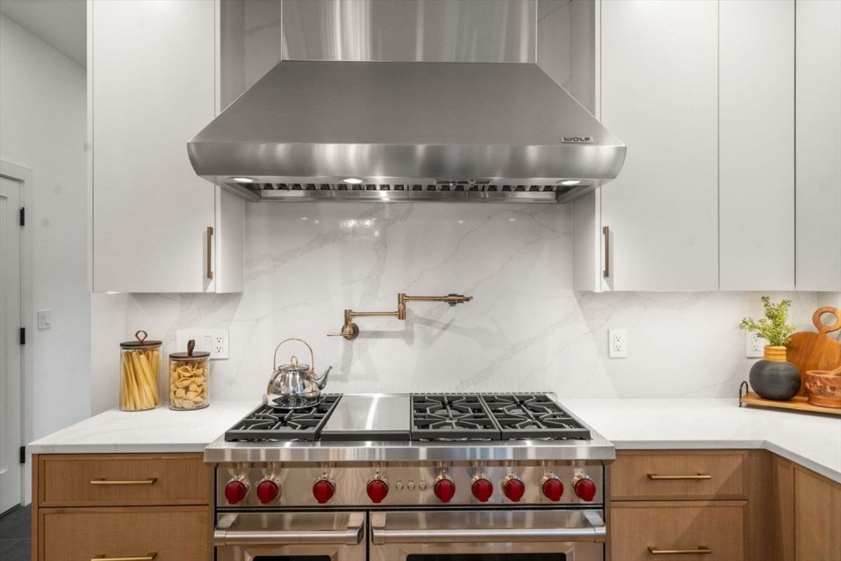 Sleek kitchen design with a professional-grade Wolf range and pot filler, accented by marble backsplash and custom cabinetry.