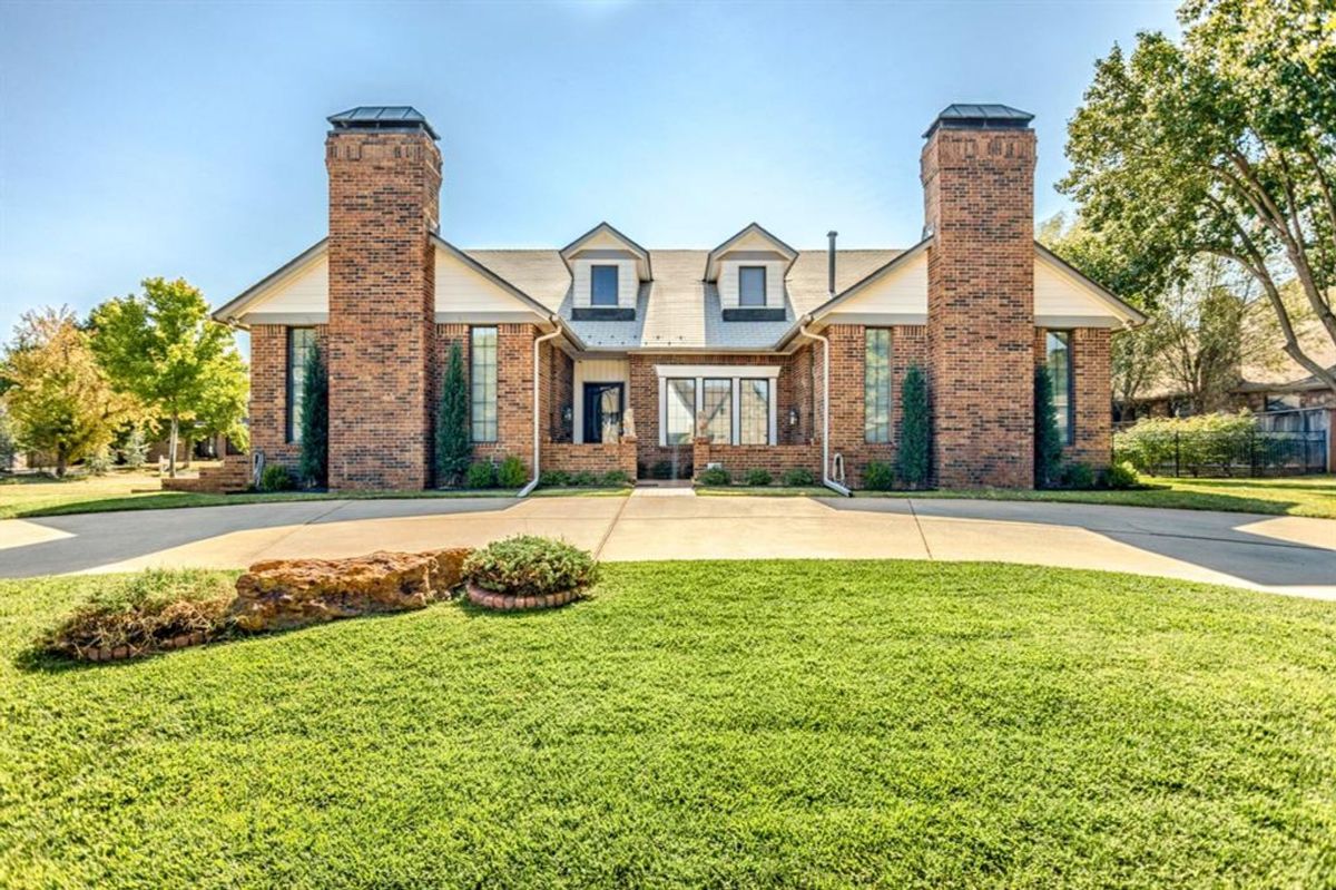 Symmetrical brick façade with prominent chimneys and dormer windows, framed by manicured landscaping.