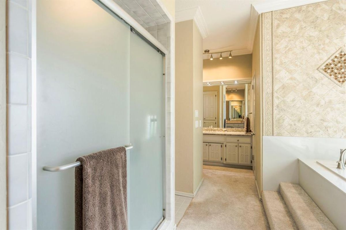 A frosted glass shower door and tiled accents complement the spacious vanity area, leading to a luxurious step-up soaking tub.