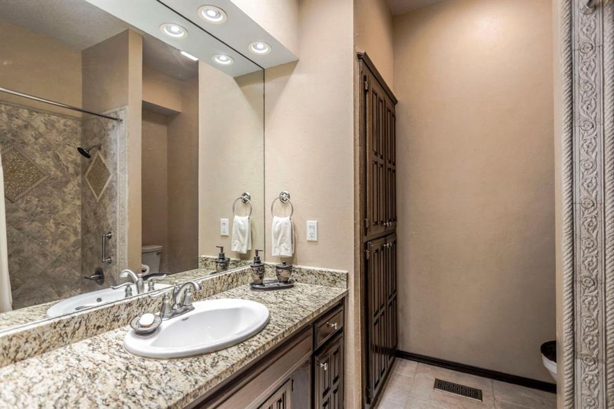 Granite countertops, tiled shower, and ample cabinetry create an elegant, functional bathroom.