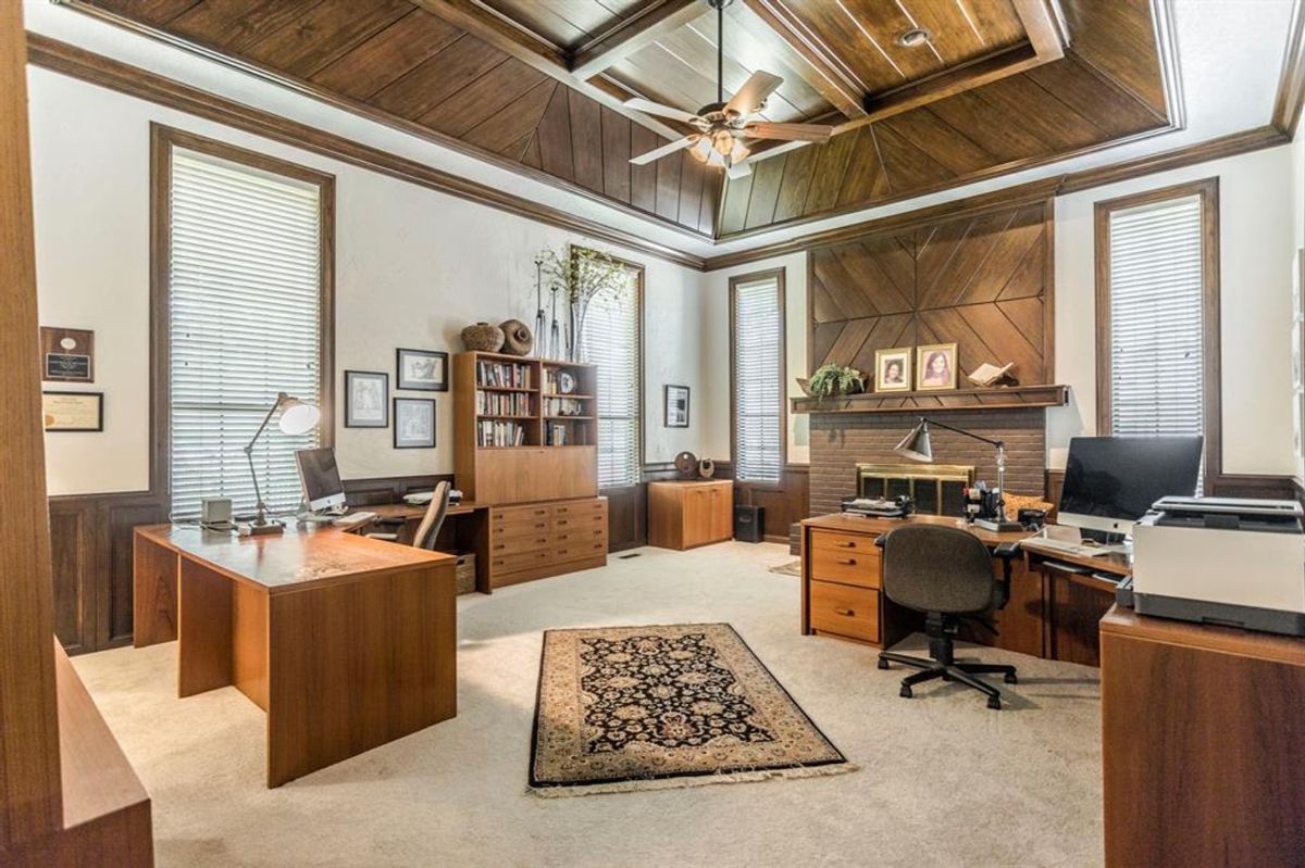 Spacious office with soaring ceilings, wood-paneled walls, built-in shelves, and a central fireplace for a refined and productive atmosphere.