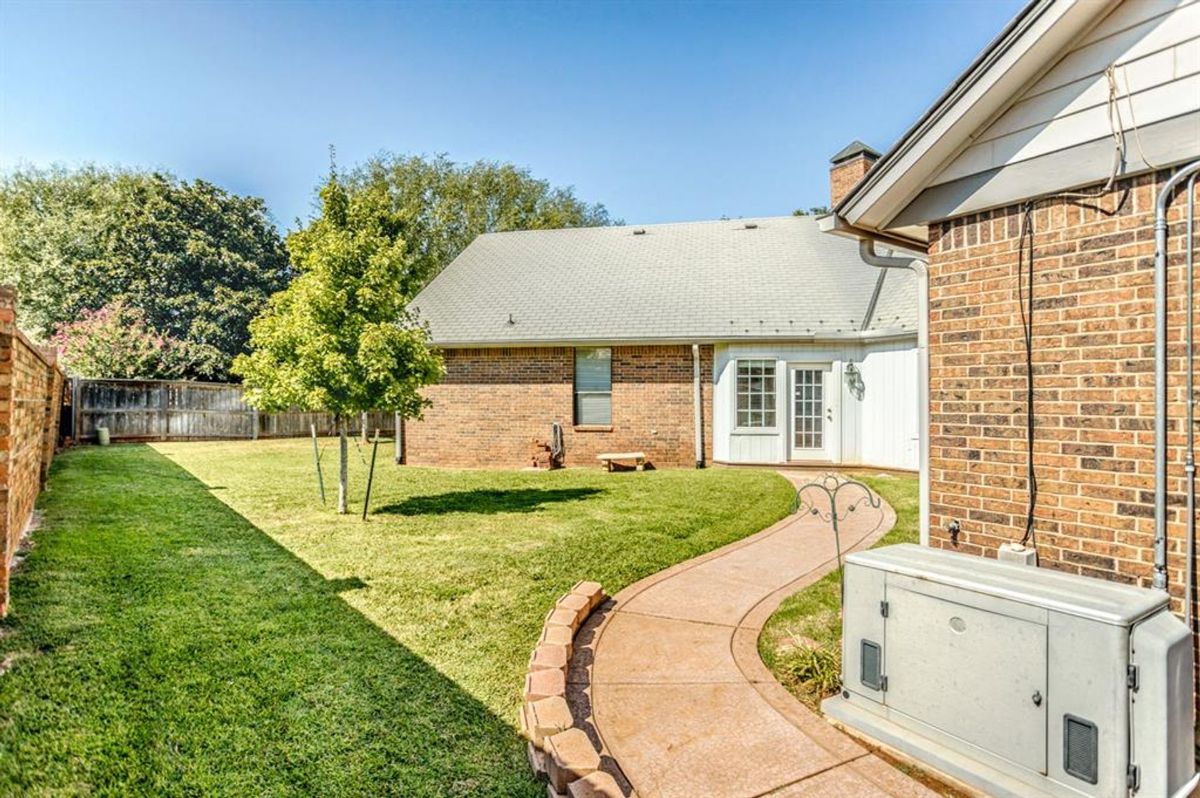 Expansive backyard featuring a paved walkway, manicured lawn, and a private corner with brick accents for added charm.