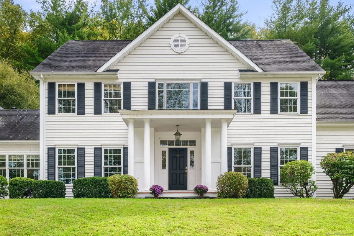 A large, two-story white colonial-style house with black shutters and a covered front porch.