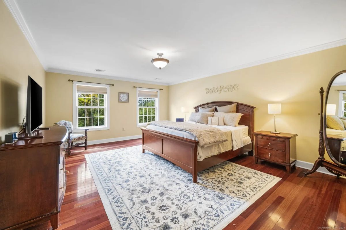 Spacious master bedroom with hardwood floors, beige walls, and a large bed with a wooden frame.