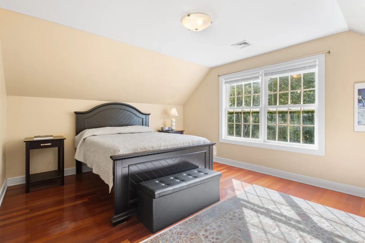 Bedroom with hardwood floors, beige walls, and a dark wood bed frame, featuring a large window that lets in plenty of natural light.