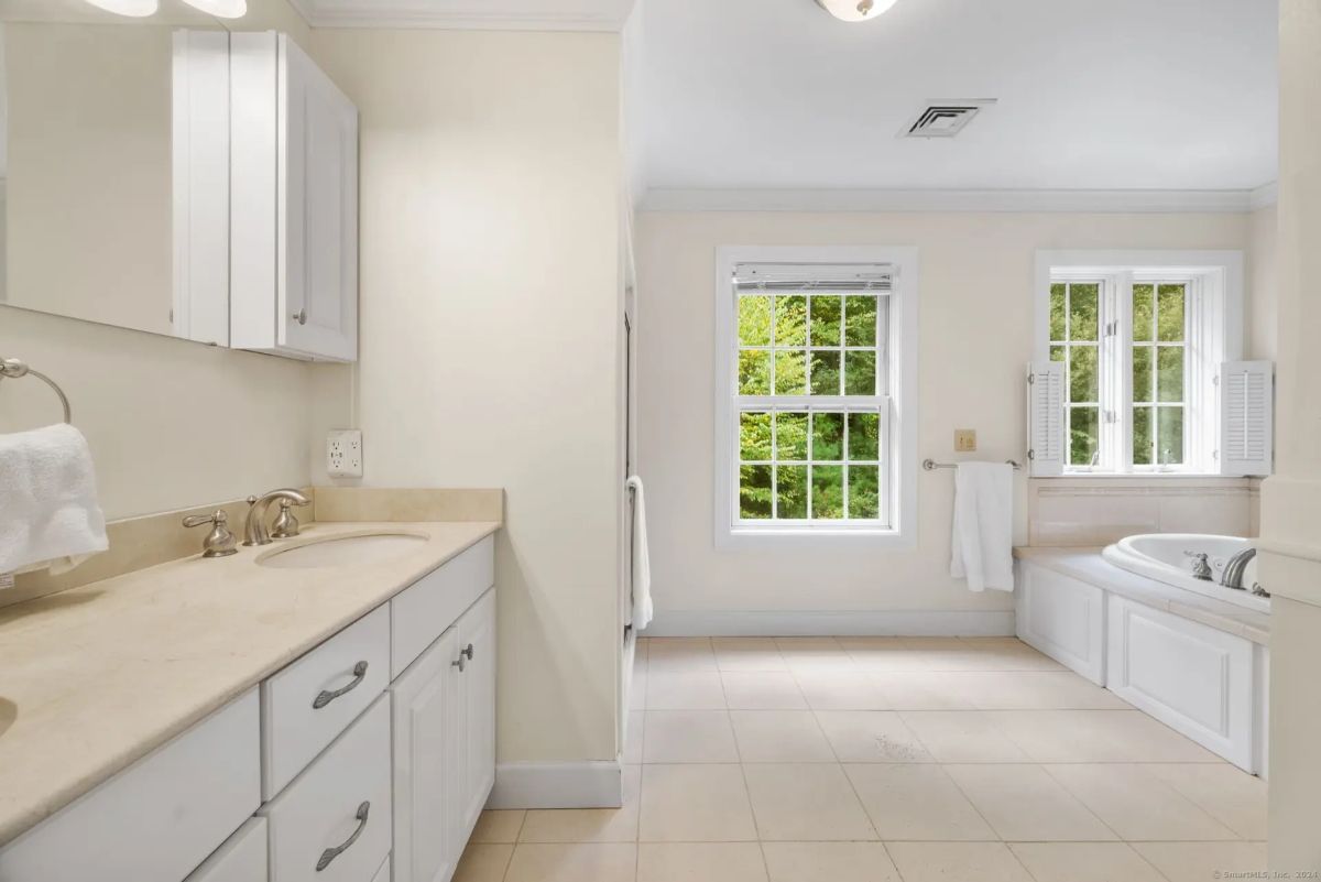 A bright and airy bathroom with a double sink vanity, a large soaking tub, and a window overlooking a wooded area.