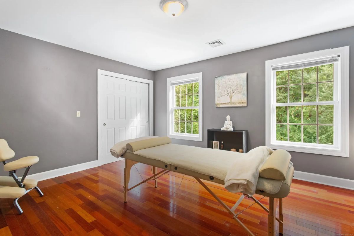 A tranquil room with hardwood floors, gray walls, a massage table, and a peaceful atmosphere, suggesting a home spa or wellness area.