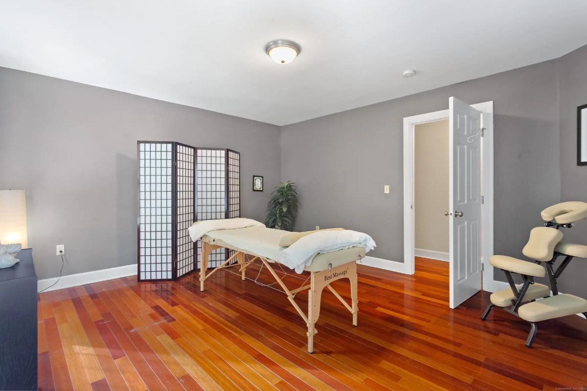 A room with hardwood floors, gray walls, a massage table, and a massage chair, suggesting a home spa or massage room.