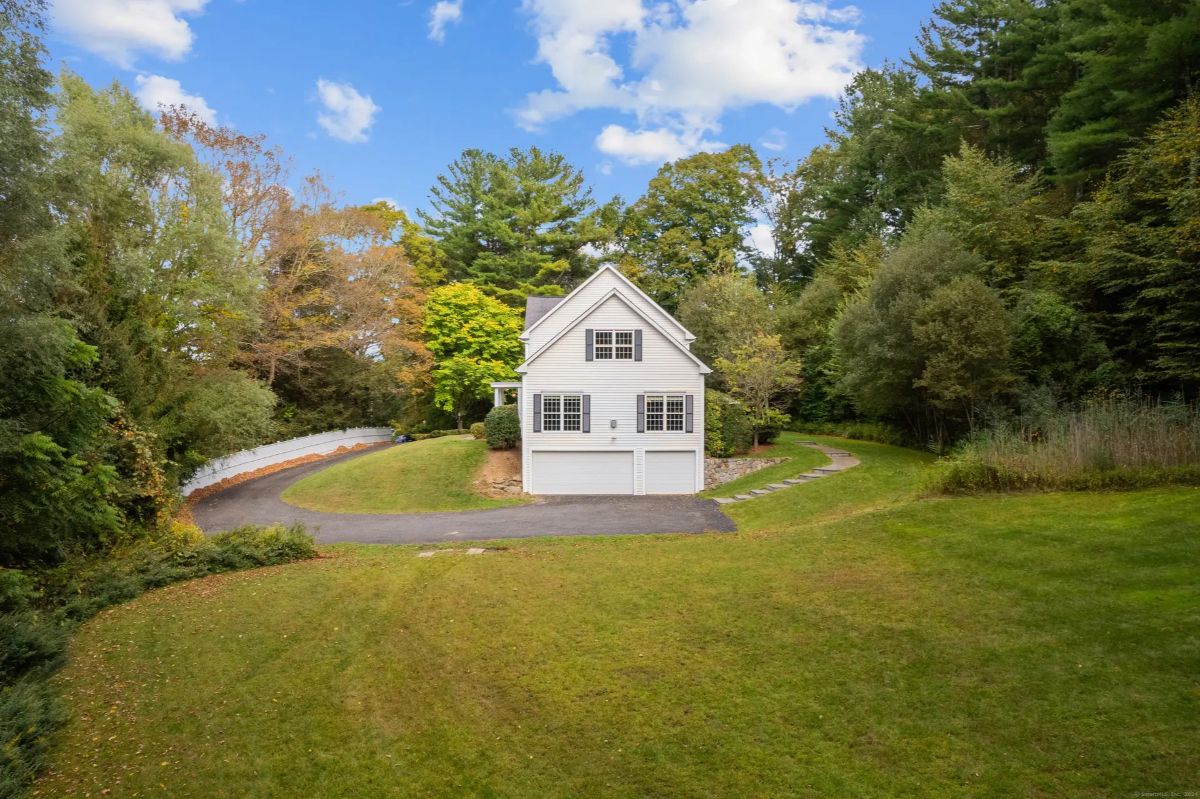 A white house with a two-car garage, surrounded by trees and a grassy lawn.