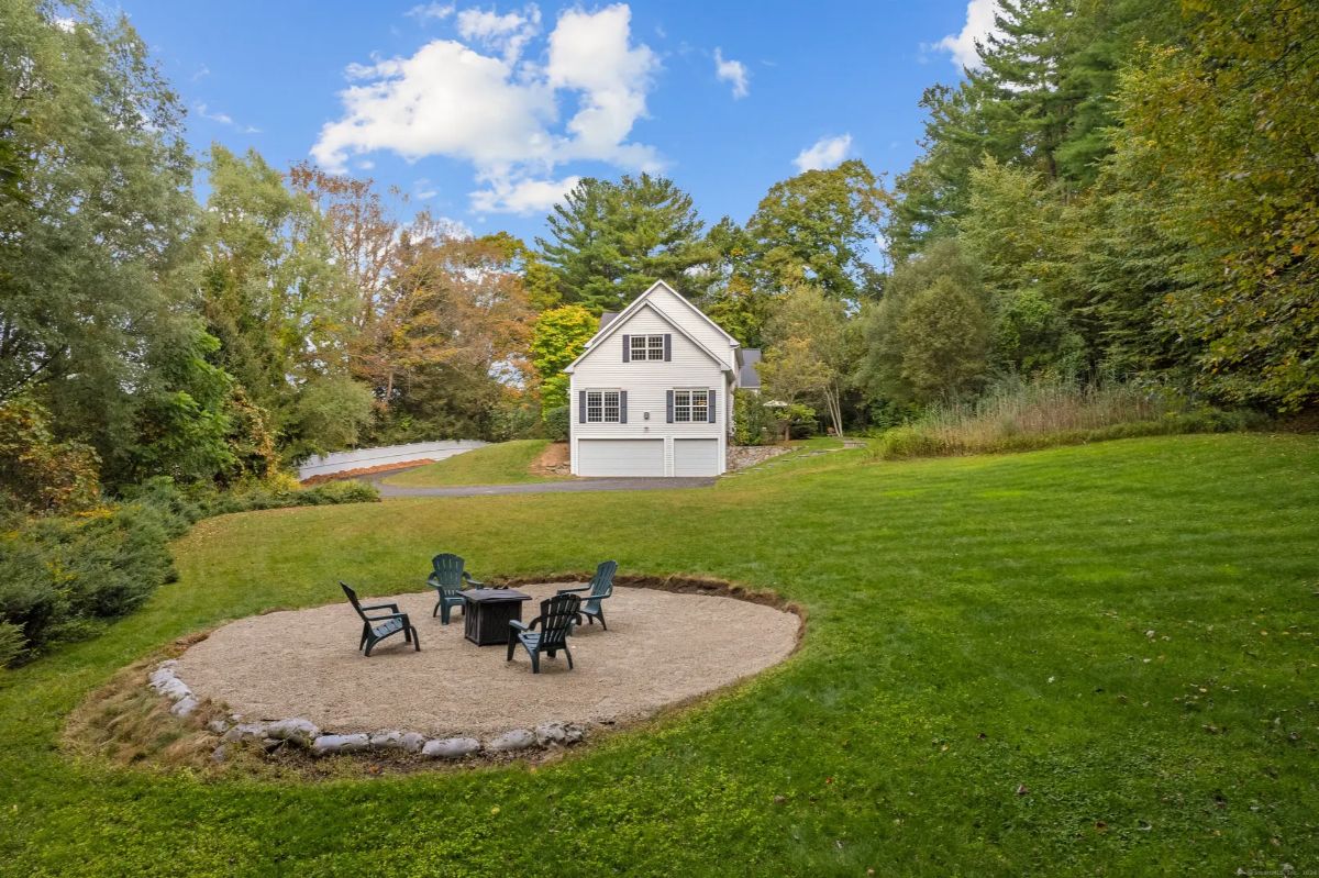 A backyard scene with a fire pit and seating area in the foreground, and a white house in the background.