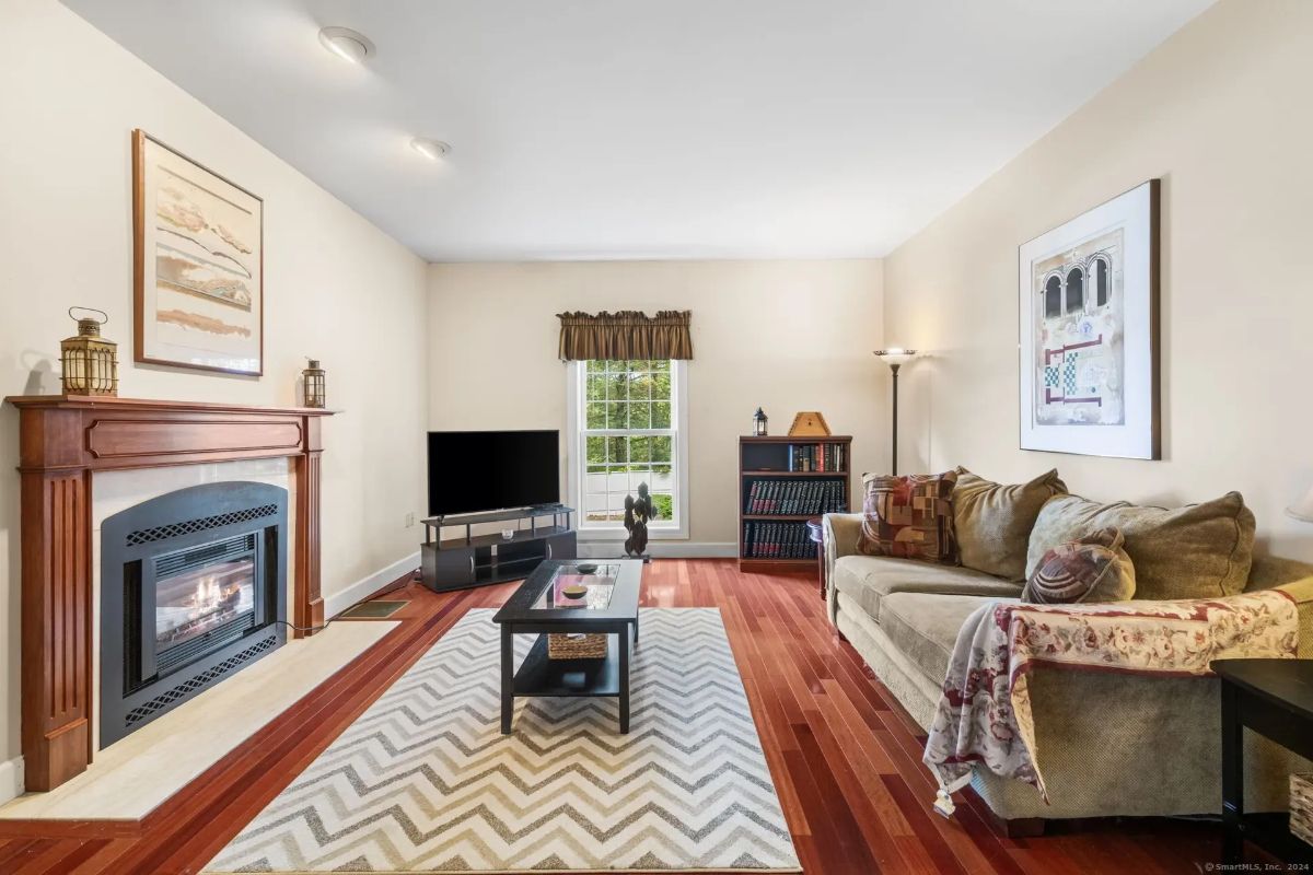 Living room featuring a gas fireplace, large window, and warm wood flooring.