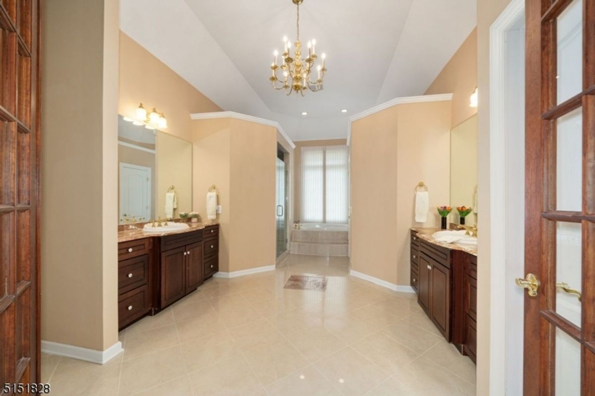 Luxurious dual vanity bathroom with a chandelier and soaking tub.