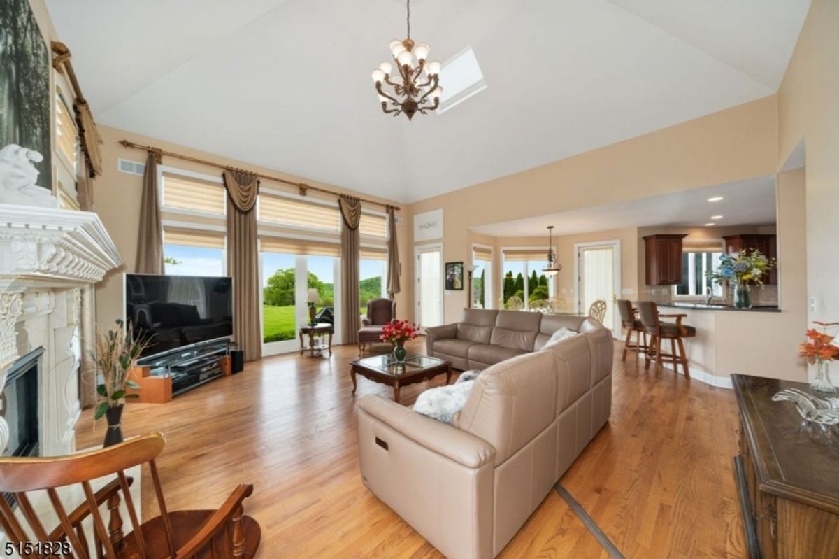 Grand living area showcasing expansive windows, a stone fireplace, and a chandelier-lit ceiling.