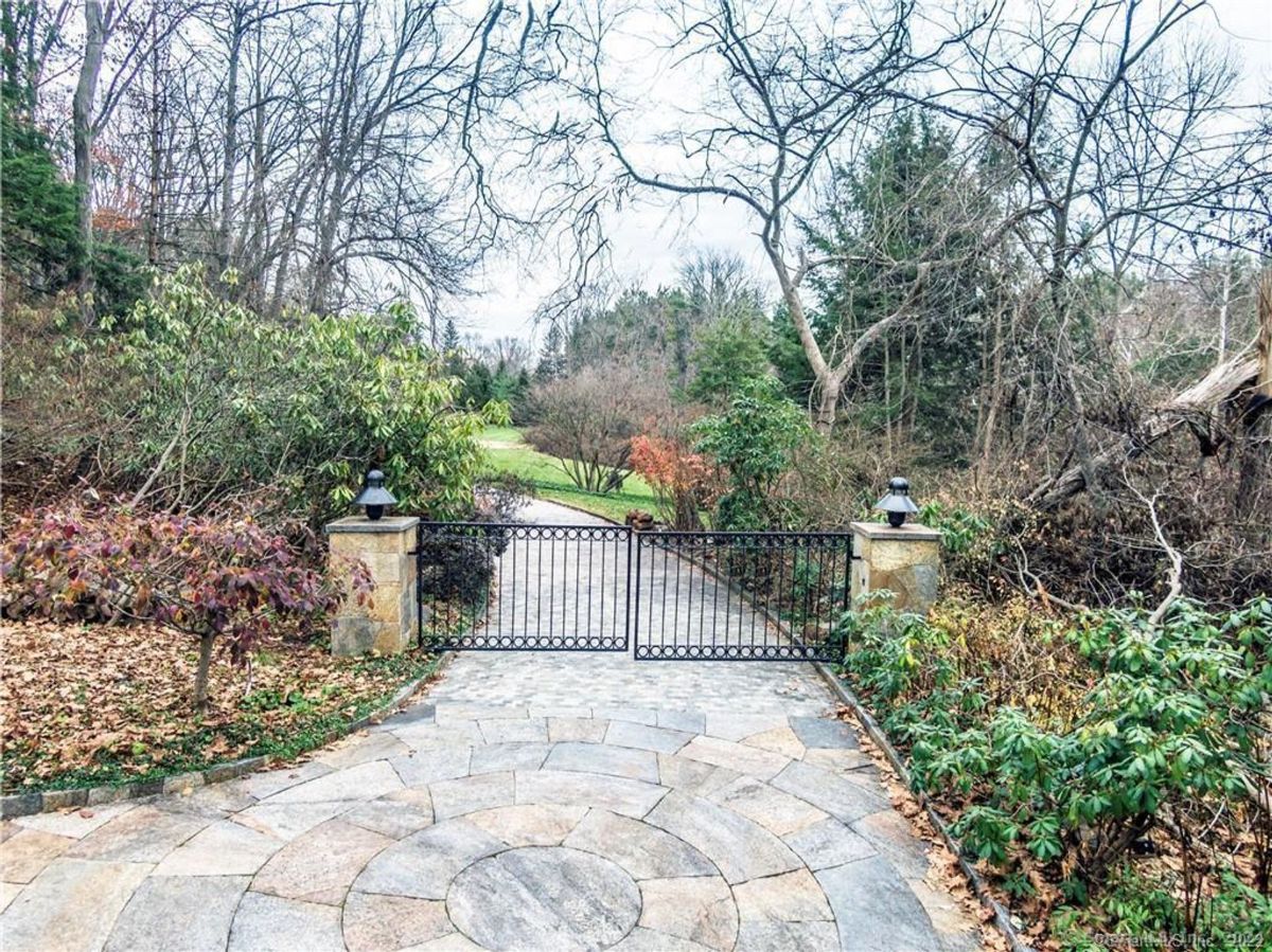 Elegant wrought-iron gate welcomes visitors to a serene garden pathway framed by lush greenery and rustic stone accents.