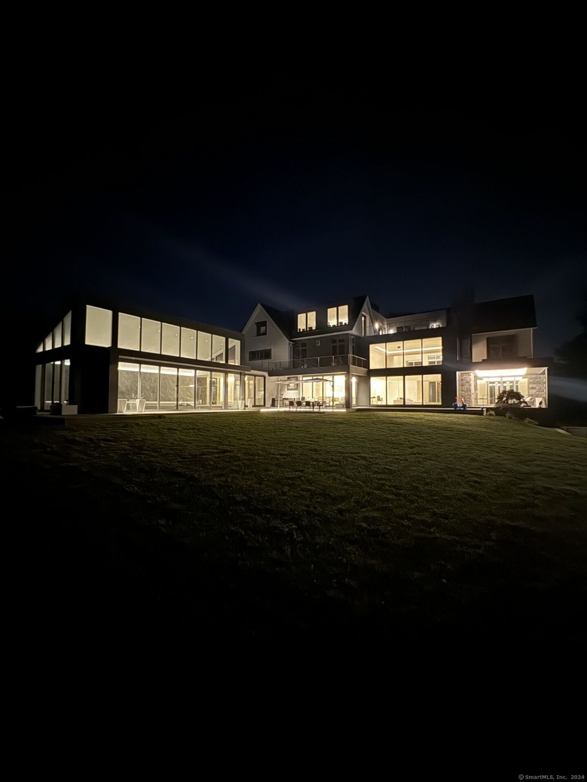 The home glows with modern elegance, its expansive glass windows illuminated against the tranquil night sky.