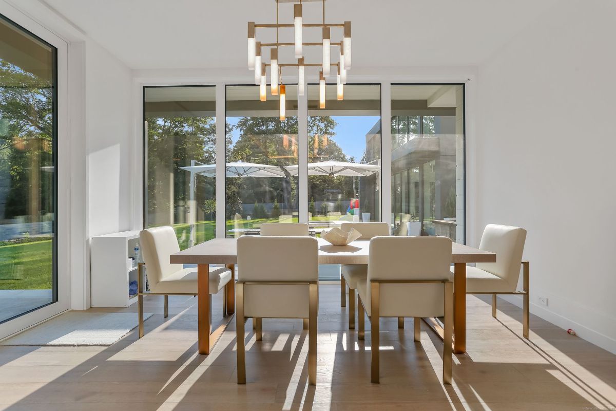 Dining area showcases elegant seating, a modern chandelier, and floor-to-ceiling glass doors that open to a lush outdoor setting.