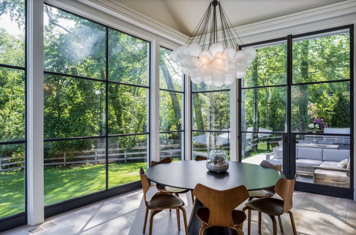 Sunlit dining area boasts a unique light fixture and expansive windows showcasing lush greenery.