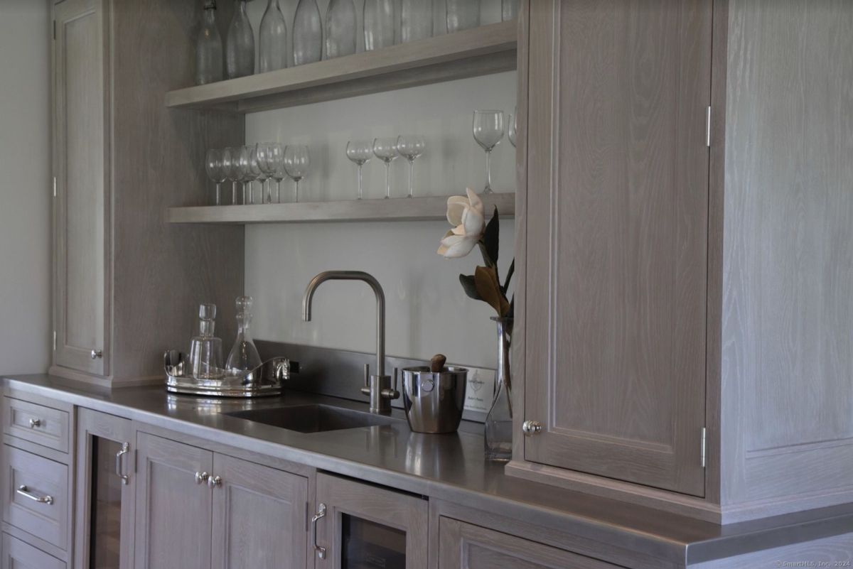 Sophisticated home bar features a sleek countertop, stylish glassware, and a single magnolia blossom.