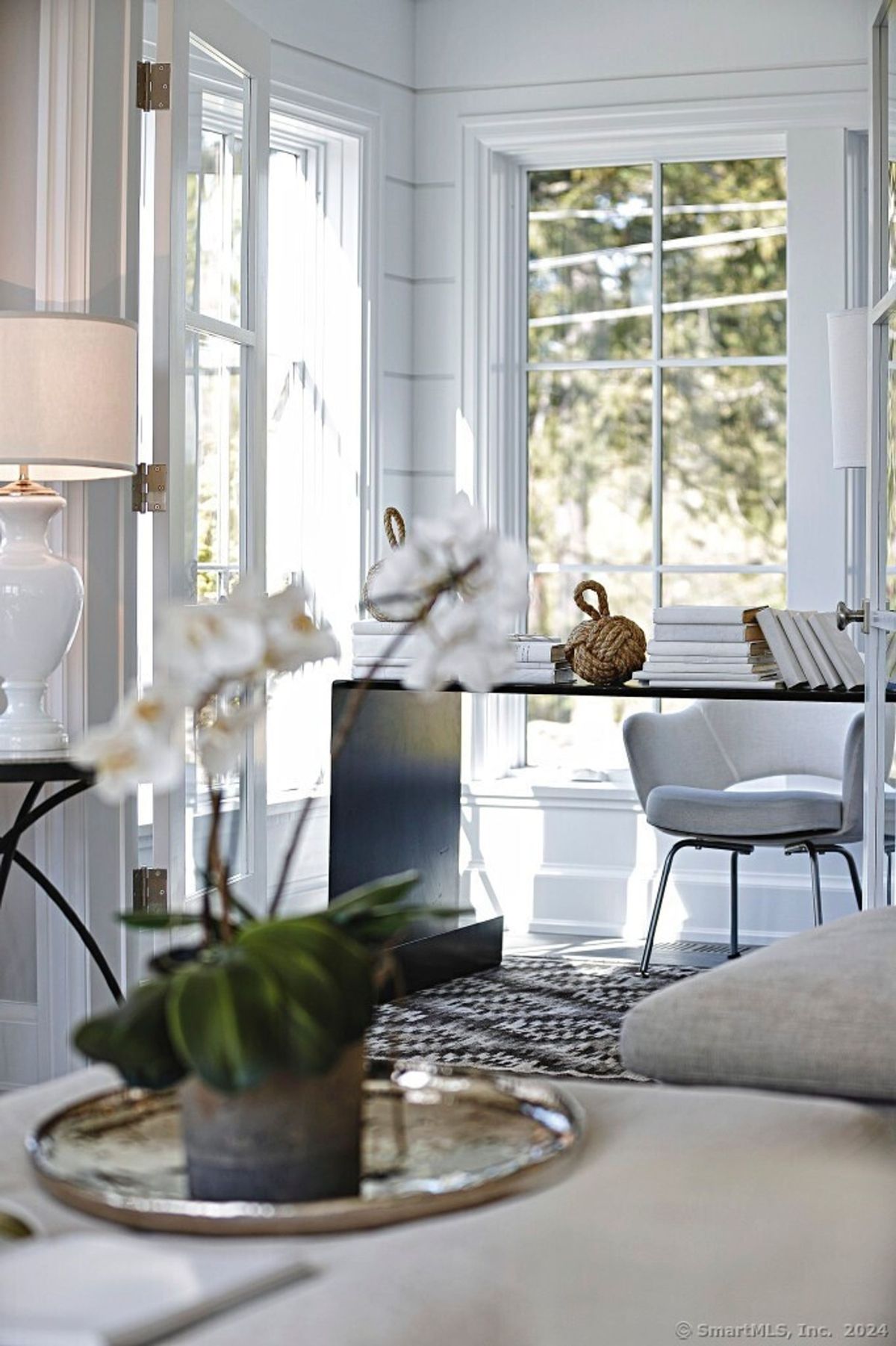 Serene sunroom workspace features a minimalist desk, white orchids, and ample natural light.