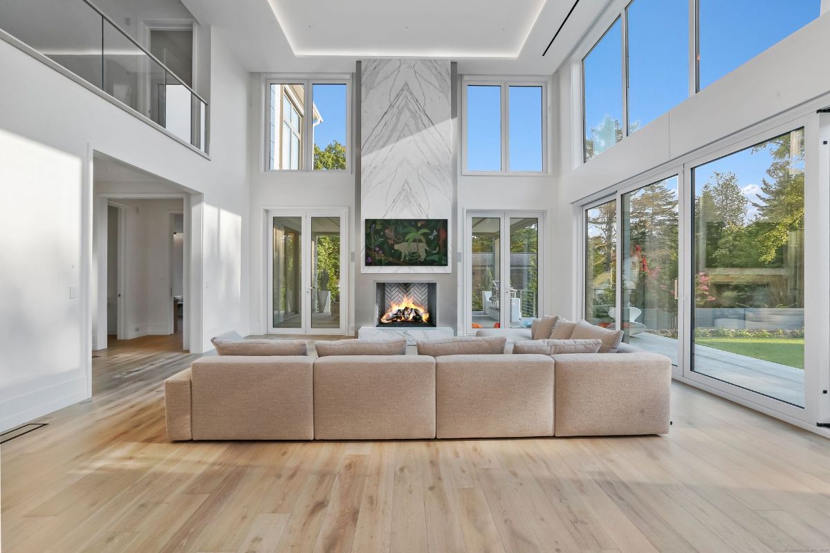 Expansive windows and a marble fireplace anchor the grand living room, blending modern elegance with inviting warmth.