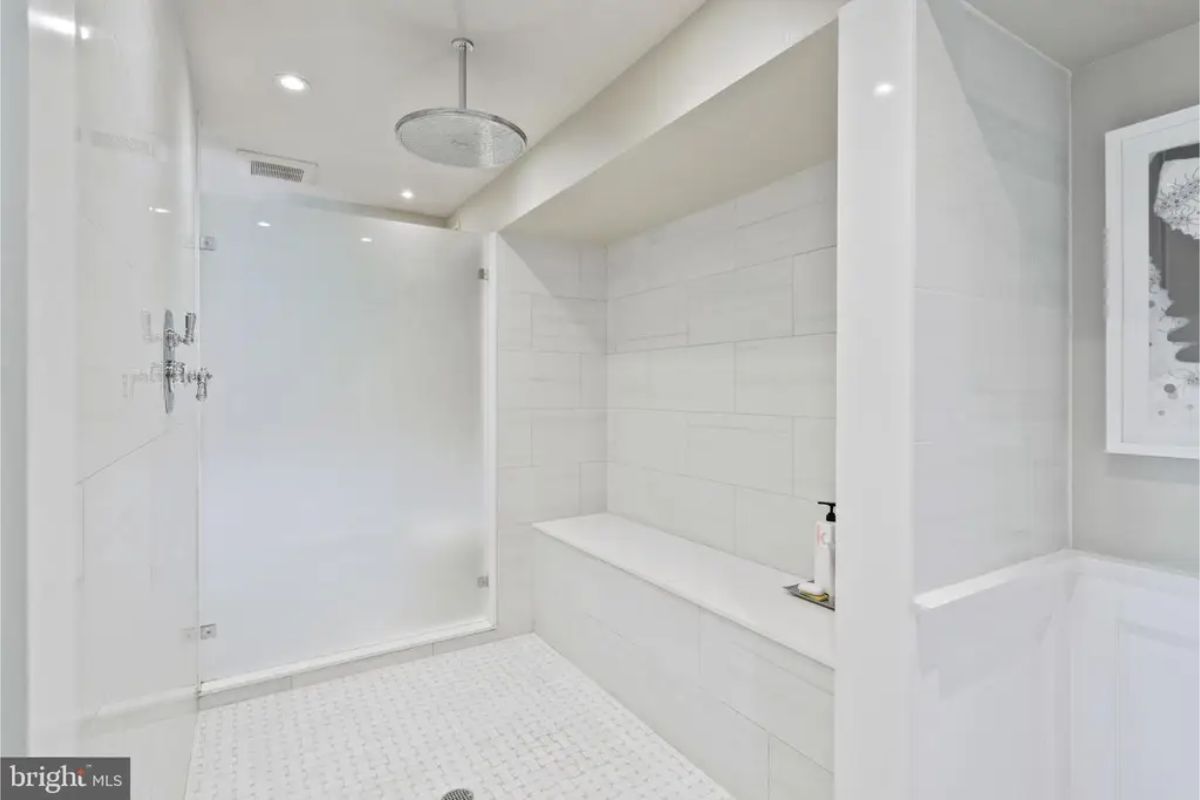 Walk-in shower features sleek white tile walls and a frameless glass divider.